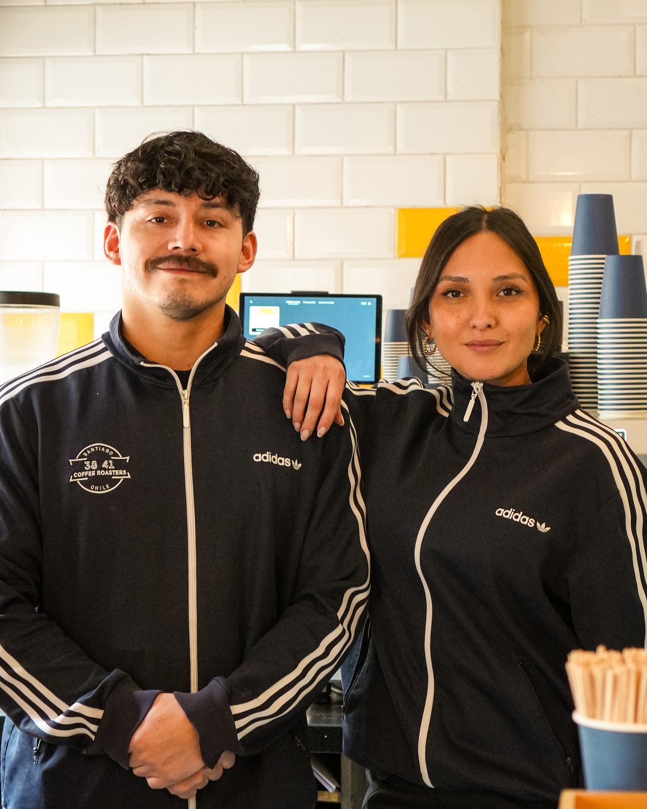 Los dueños de 38 41 Coffee Roasters tras el mesón de la cafetería, con la máquina de café y las tazas apiladas al fondo.